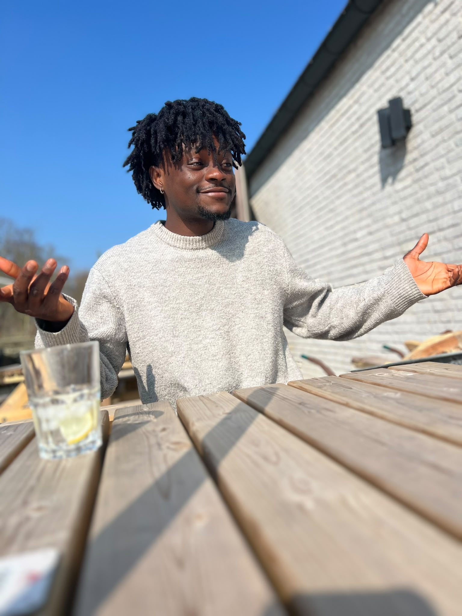 Man sitting outdoors at a table, gesturing open-handed while reflecting on finding his why